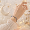 Hand wearing a blue aquamarine bracelet with feather charm background featuring stars and a moon.
