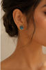 Close-up of an ear wearing a gold earring with abalone shell on a neutral background