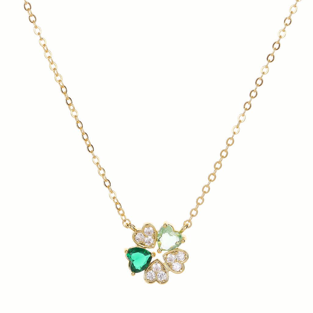 Gold necklace with a clover-shaped pendant featuring green crystals on a white background